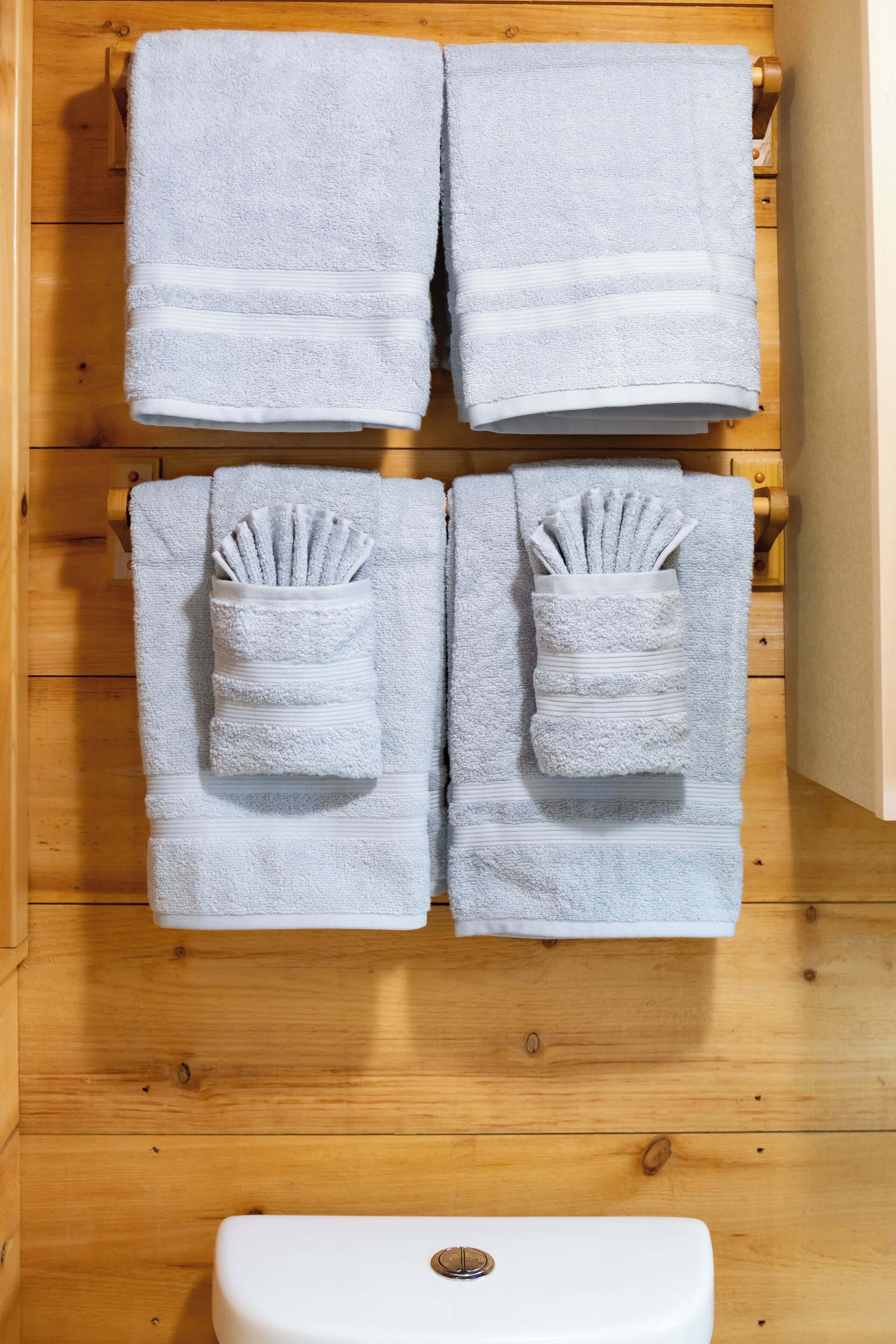 A bathroom with wooden walls, a white toilet, and four towels neatly hung on towel racks.