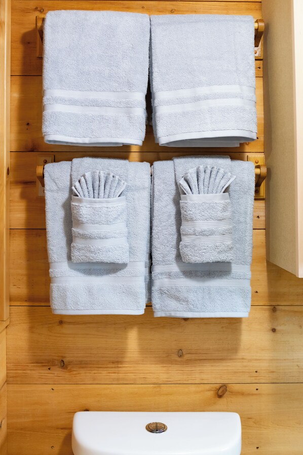 A bathroom with wooden walls, a white toilet, and four towels neatly hung on towel racks.