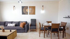 A living room with a sofa, armchair, dining table, chairs, and wall art. - Peaceful place near stadium and airport (Tanger)