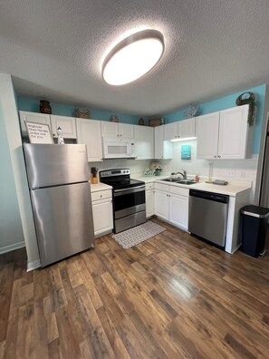 A modern kitchen with white cabinets, stainless steel appliances, and a wooden floor. - Young's Plantation Paradise-steps away from beach (Gulf Shores)