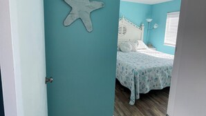 Una stanza dalle pareti color acquamarina, con una decorazione a stella marina, un letto con copriletto fantasia e pavimento in legno.
