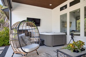 A modern outdoor seating area with a wicker chair, a hot tub, and a mounted telescope. - Luxe Retreat w/Hot Tub, Patio, Fenced Yard! (Lago Vista)