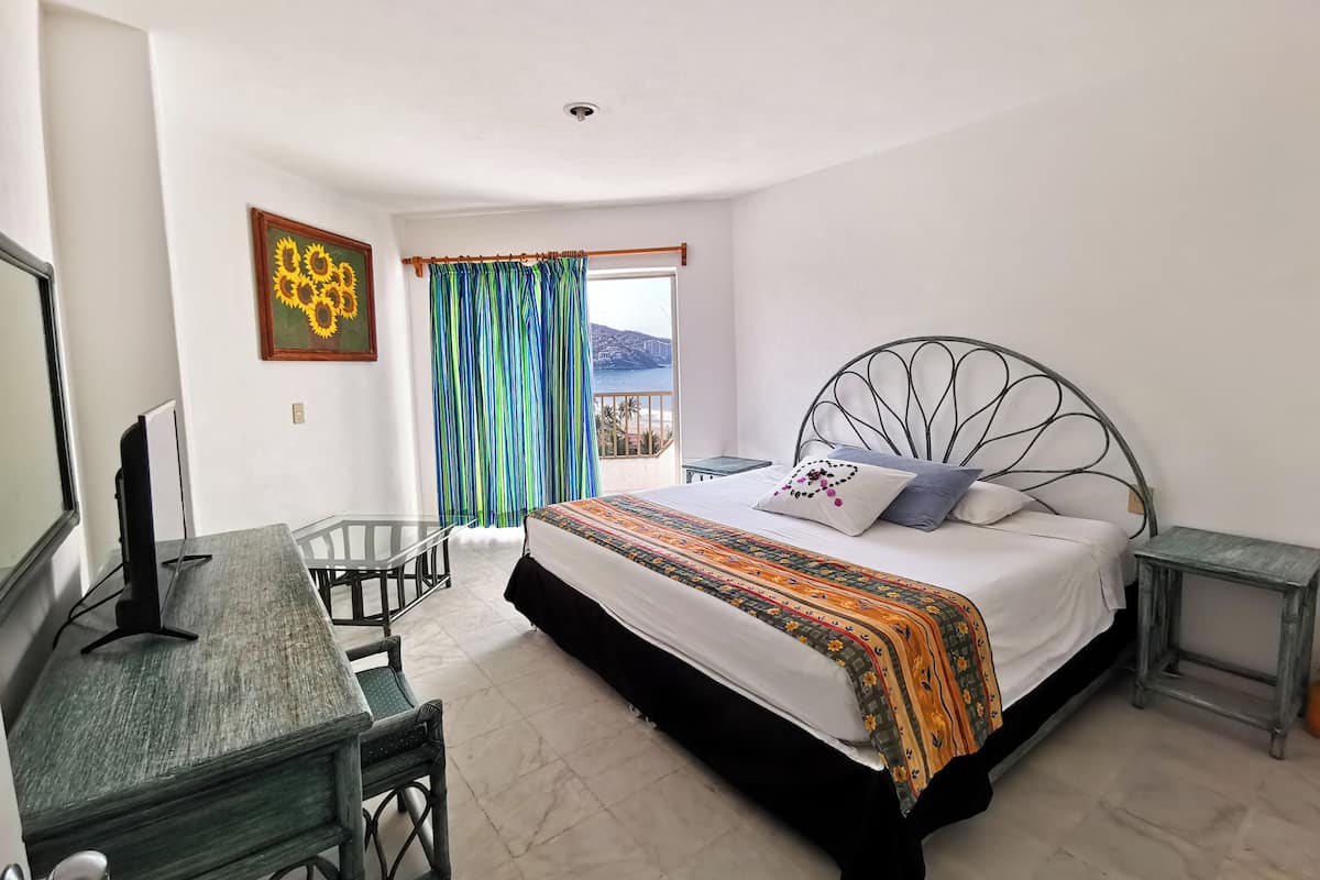 Un dormitorio con cama, escritorio, silla, televisor y ventana con cortinas.