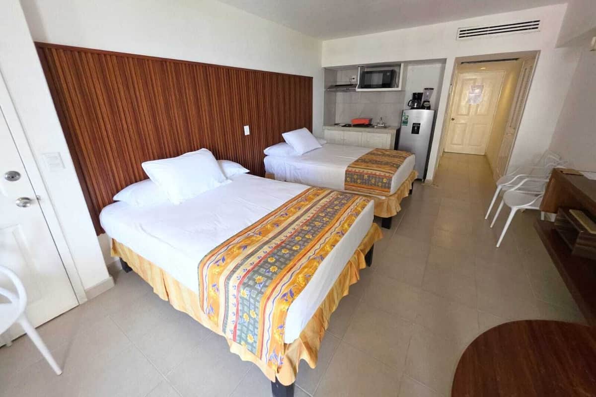 Habitación de hotel con dos camas, kitchenette, microondas, refrigerador y una puerta que da a otra habitación.