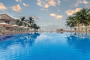 A swimming pool with lounge chairs and umbrellas, surrounded by palm trees and a building with a tiled roof. - Condominios Torre Continental Ixtapa (Ixtapa)