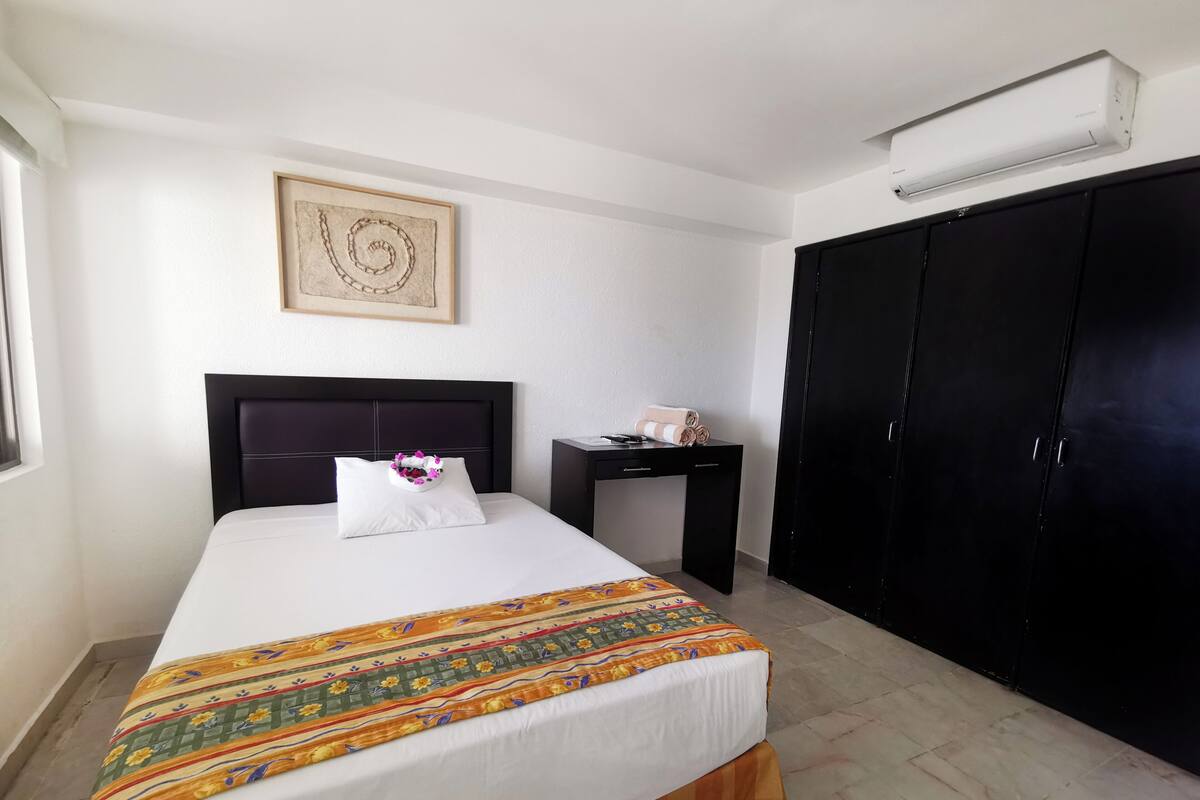 Habitación de hotel con cama, escritorio, armario y aire acondicionado de pared.