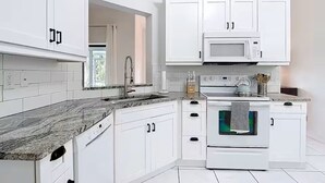 Une cuisine moderne avec des meubles blancs, un plan de travail en granit, un four à micro-ondes, un four traditionnel et une fenêtre avec des rideaux.