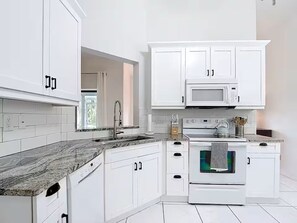 A modern kitchen with white cabinets, a granite countertop, a microwave, an oven, and a window with curtains. - Lake Side Spa Home (Naples)