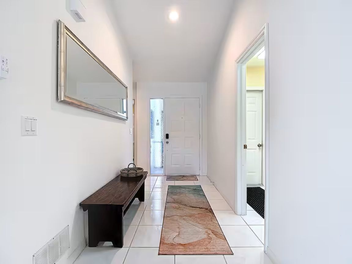 Un couloir avec un banc, un miroir, une porte et un tapis.