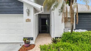 Une maison d’habitation avec un garage, une porte d’entrée et un petit jardin agrémenté d’un palmier et de plantes en pot.