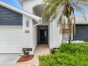 Ein Wohnhaus mit Garage, Eingangstür und kleinem Garten mit einer Palme und Kübelpflanzen.
