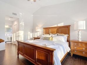 Um quarto com cama de madeira, mesas de cabeceira, cômoda e um espelho sobre a cama.