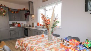Cozinha com armários cinza, uma mesa de jantar com toalha florida e uma janela com decoração de aniversário.