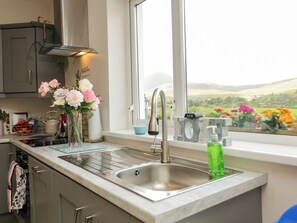 Una cocina con un lavamanos de acero inoxidable, una ventana con vista a un jardín y un florero con flores sobre la encimera.