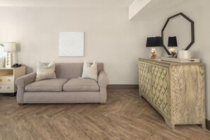 A neutral-toned living room with a sofa, a wooden cabinet, a framed artwork, and a lamp.
