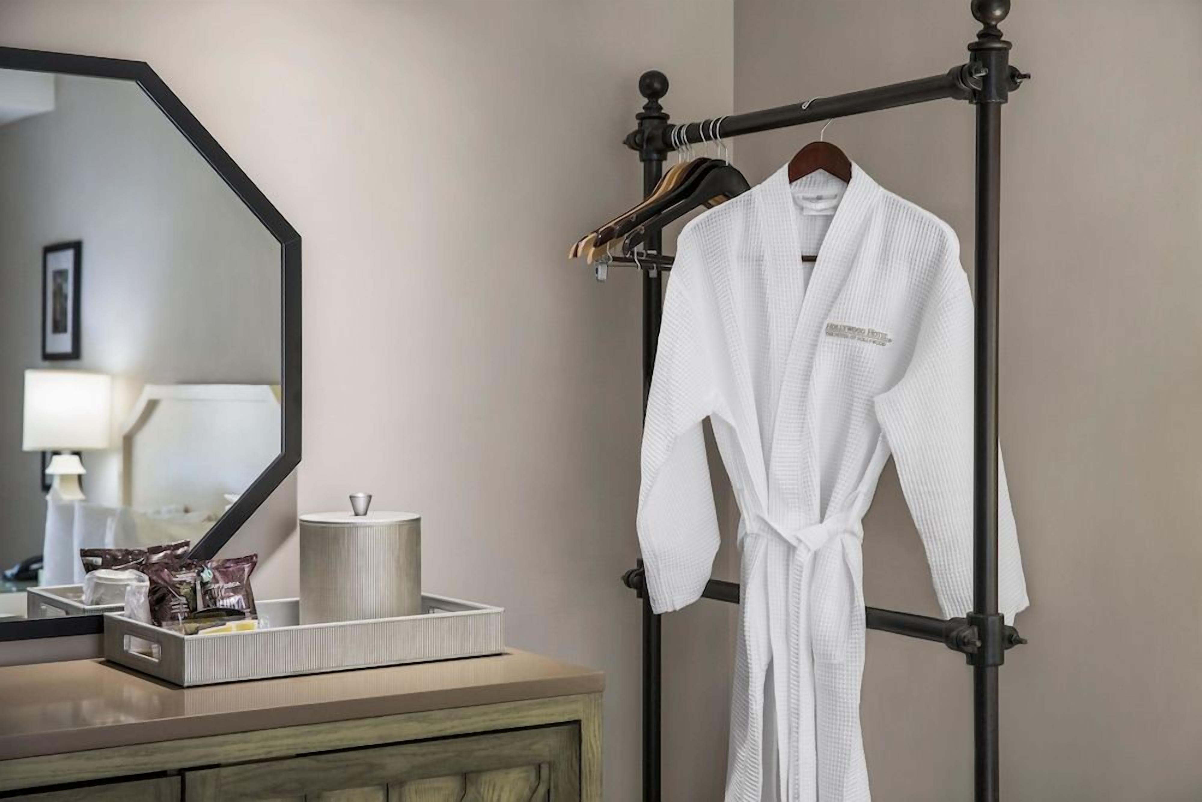 Ein Badezimmer mit Spiegel, Handtuchhalter und einem weißen Bademantel sowie Pflegeprodukten auf einem Tablett.