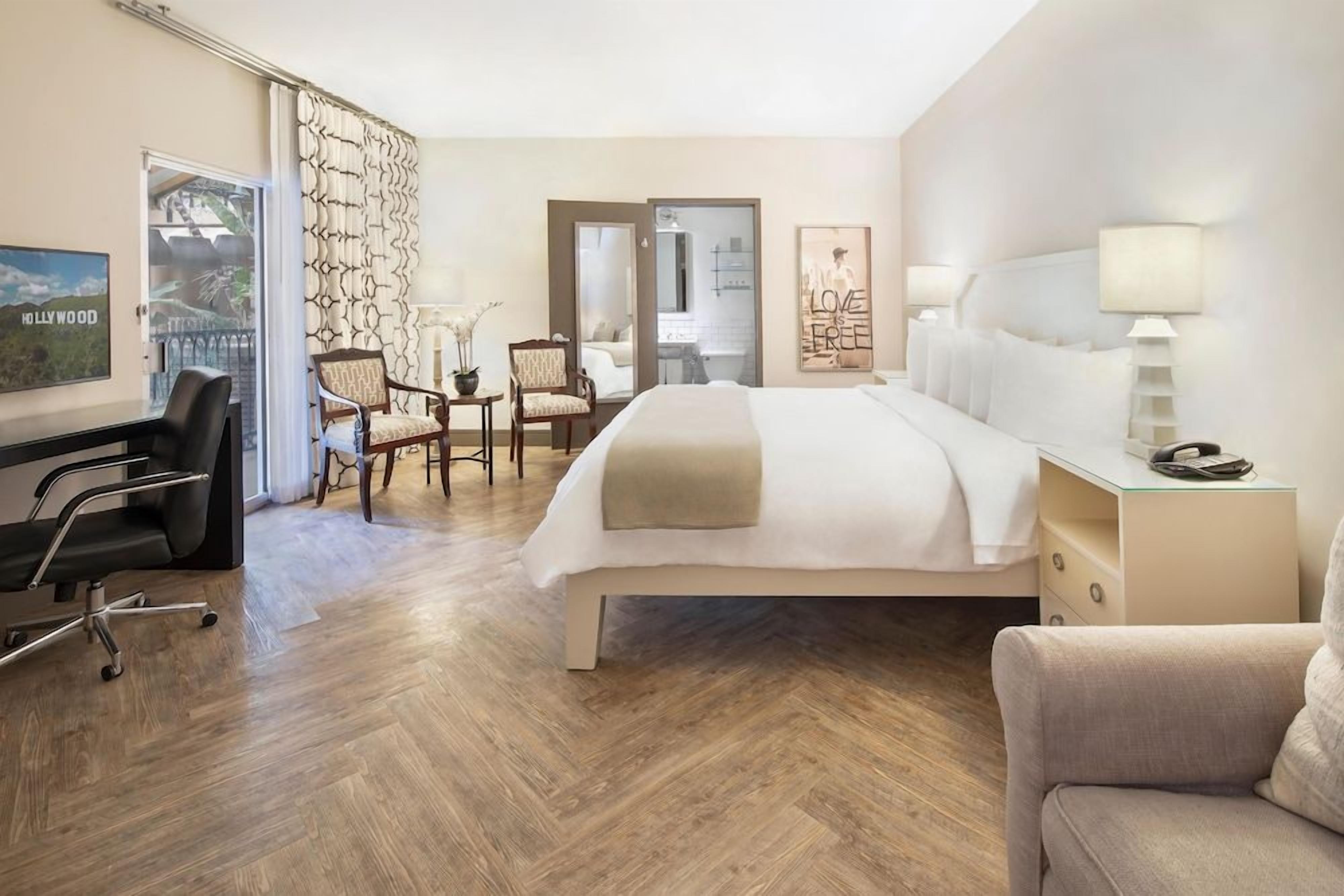 Ein Hotelzimmer mit einem großen Bett, einem Schreibtisch, zwei Stühlen, einem Nachttisch und Blick ins Freie.