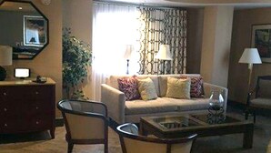 A living room with a sofa, two armchairs, a coffee table, a TV, and a lamp.