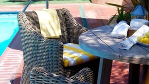A poolside area with wicker chairs, a table with a bowl of lemons, and an umbrella.