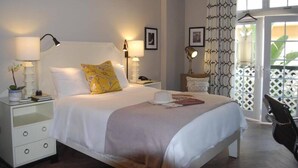A neatly arranged bedroom with a bed, bedside lamps, a nightstand, and a view through a window.