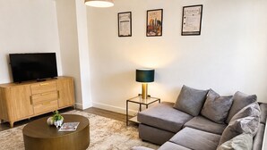 Ein Wohnzimmer mit einer Couch, einem Couchtisch, einem Fernseher auf einer Holzkommode und gerahmten Bildern an der Wand.