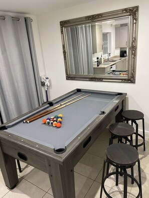 Uma mesa de bilhar com bolas, um espelho e três banquetas.