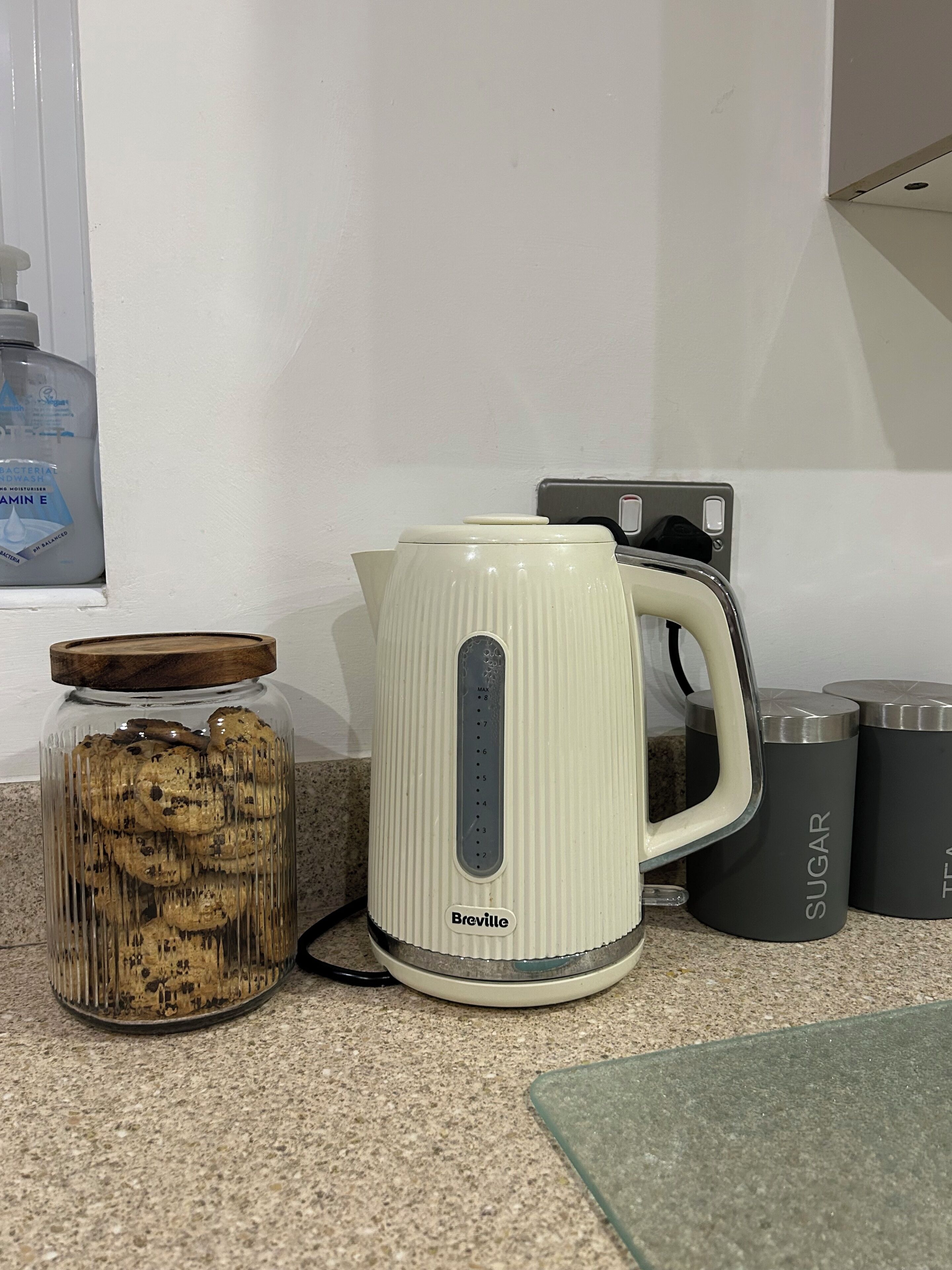 A kitchen counter with a Breville kettle, a jar of cookies, and two stainless steel containers labeled 'SUGAR' and 'TEA'.