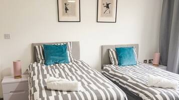 Een hotelkamer met twee bedden, een nachtkastje, een lamp en twee foto's in lijsten aan de muur.