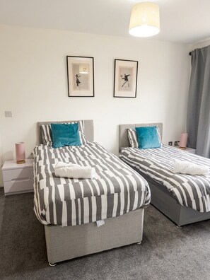 A hotel room with two beds, a nightstand, a lamp, and two framed pictures on the wall. - 3 bed home near Etihad and Co-op live with parking (Manchester)
