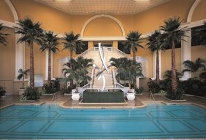 Un área de piscina con palmeras, una escalera central y suelo de baldosas.