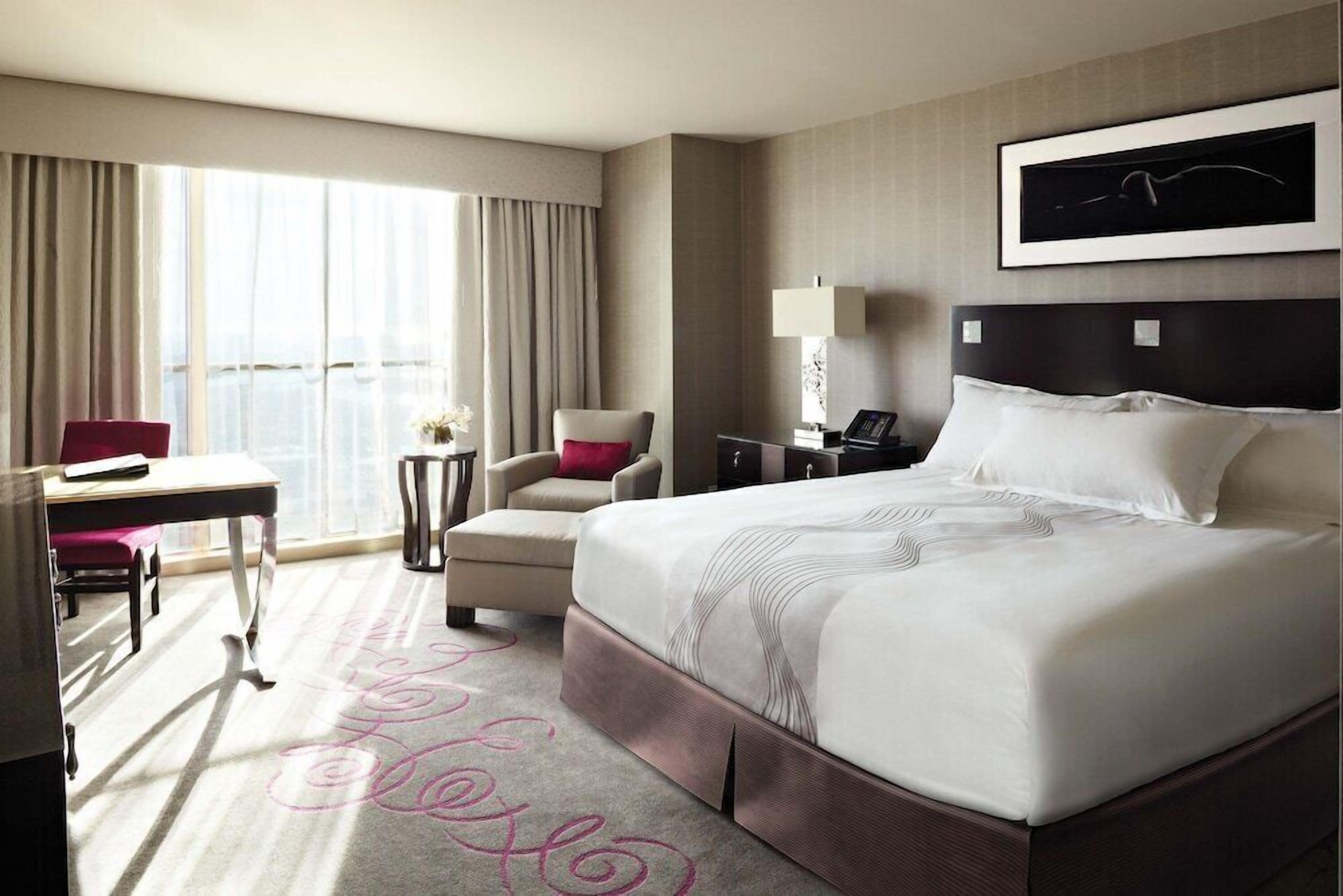 A hotel room with a large bed, a desk, a chair, a lamp, and a window with curtains.