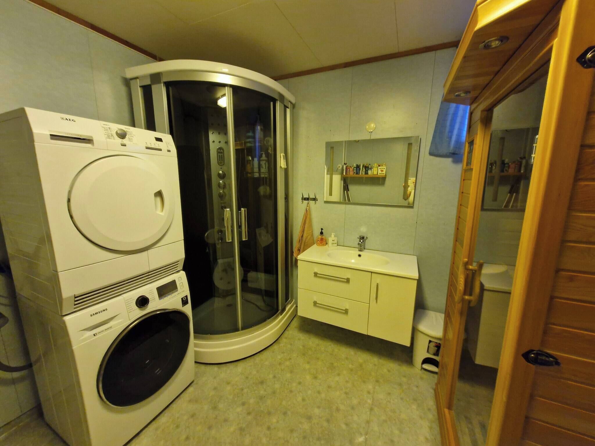 Un baño compacto con lavadora, cabina de ducha de cristal y lavabo con espejo arriba.