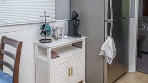 Une cuisine compacte équipée d’un réfrigérateur, d’une machine à café et d’une fenêtre avec des stores.