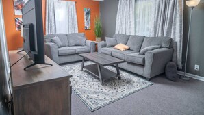 Un salon avec deux canapés gris, une table basse, un téléviseur posé sur un meuble et un tapis à motifs.