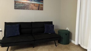 A room with a black sofa, a green ottoman, and a painting of a beach scene. - Hidden Gem Sarasota Getaway Near Siesta Key (Sarasota)