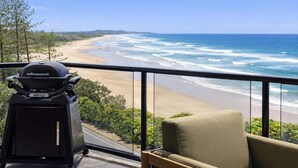 A balcony with a view of a beach and ocean, a grill, and a chair. - Summer Cove - Beachfront with Pool (Sunshine Coast)