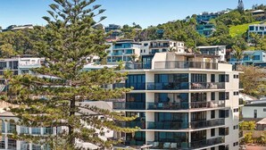 A multi-story building with balconies, large windows, and a view of surrounding residential buildings. - Summer Cove - Beachfront with Pool (Sunshine Coast)