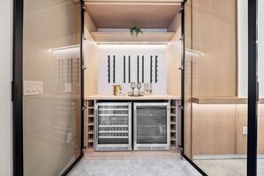A modern closet with two glass-fronted mini-fridges, a wooden shelf with decorative items, and a wall-mounted light fixture. - 10BR house sleeps 24 with pool and game room (Clermont)
