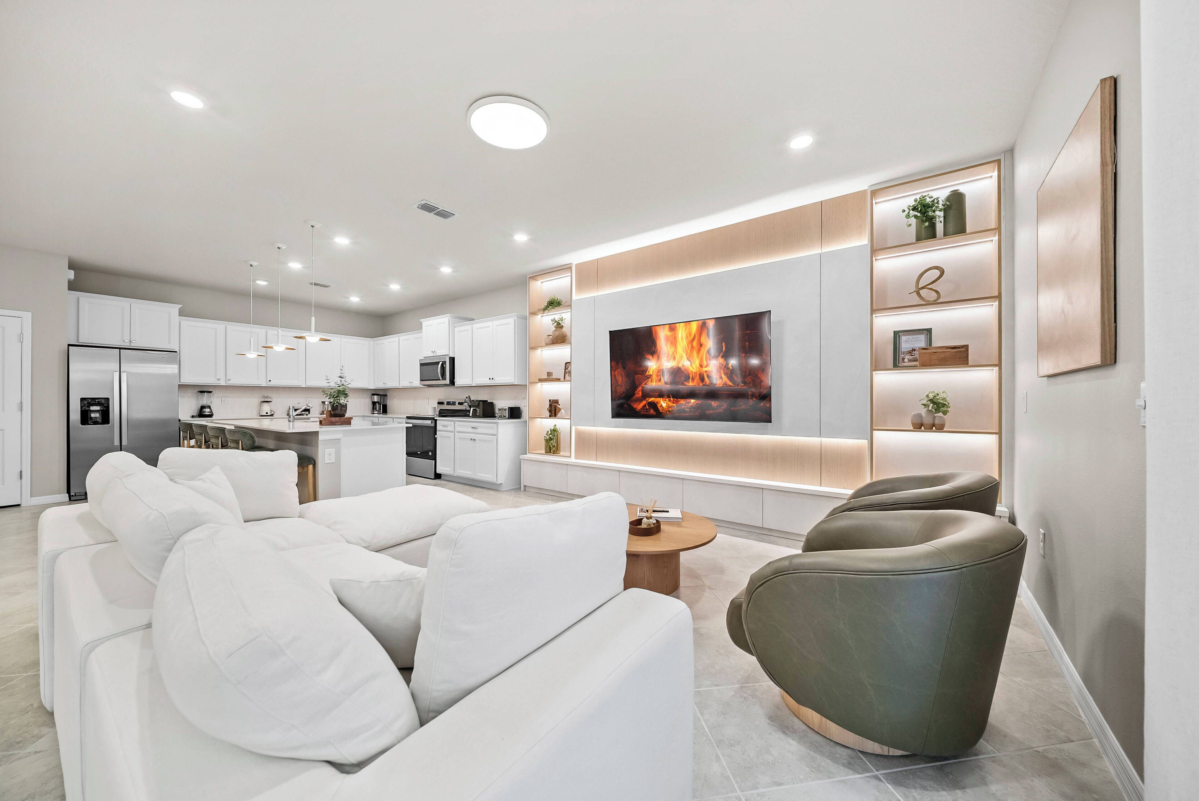 A modern living room with a white sofa, a green armchair, a flat-screen TV, and a fireplace.