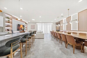 A modern kitchen with a central island, bar stools, a dining table with chairs, pendant lighting, and a large window with sheer curtains. - 10BR house sleeps 24 with pool and game room (Clermont)