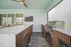 Une cuisine moderne dotée d’un barbecue intégré, de meubles en bois et d’une grande fenêtre donnant sur un quartier résidentiel.