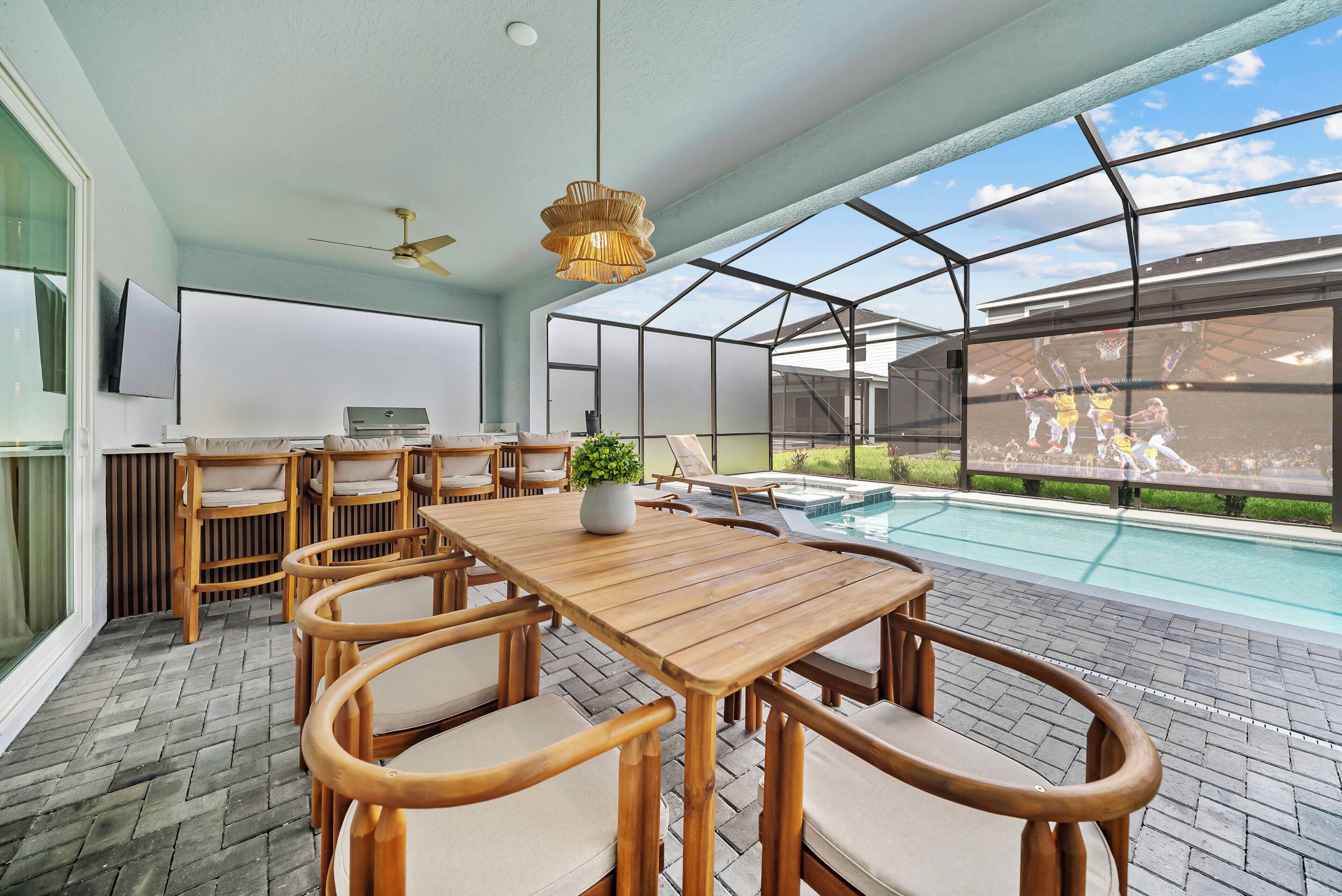 A spacious room with a wooden dining table, wicker chairs, a ceiling fan, a large window, and a view of a swimming pool.