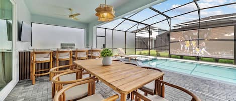 A spacious room with a wooden dining table, wicker chairs, a ceiling fan, a large window, and a view of a swimming pool.