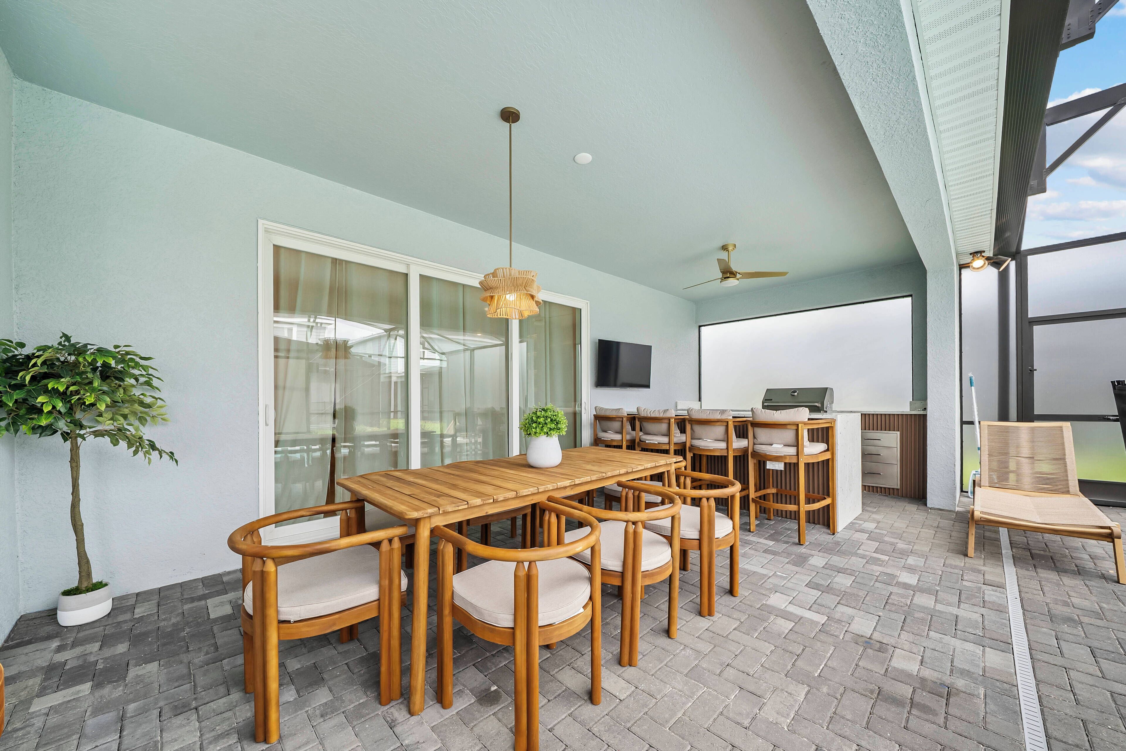 An outdoor patio with a wooden table and chairs, a ceiling fan, and a TV mounted on the wall.