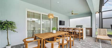 Un patio exterior con mesa y sillas de madera, un ventilador de techo y un televisor montado en la pared.