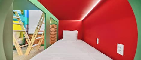 Una habitación con cama, pared roja y vistas a un área de juegos colorida.