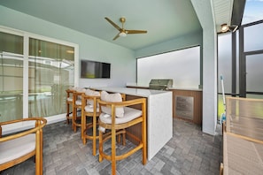 A balcony with a bar area, wooden chairs, a ceiling fan, and a TV screen. - 10BR house sleeps 24 with pool and game room (Clermont)
