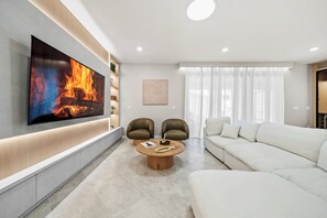 Ein modernes Wohnzimmer mit Flachbildfernseher, zwei Ledersesseln, einem runden Couchtisch und einem weißen Sofa.