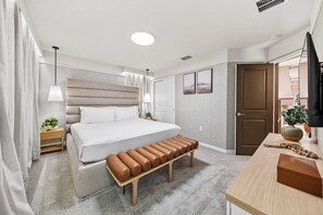 A modern hotel room with a bed, a bench, a desk, and a TV. - 10BR house sleeps 24 with pool and game room (Clermont)