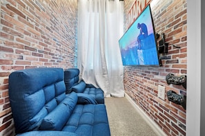 A room with a brick wall, a flat-screen TV, a blue sofa, and a curtain. - 10BR house sleeps 24 with pool and game room (Clermont)